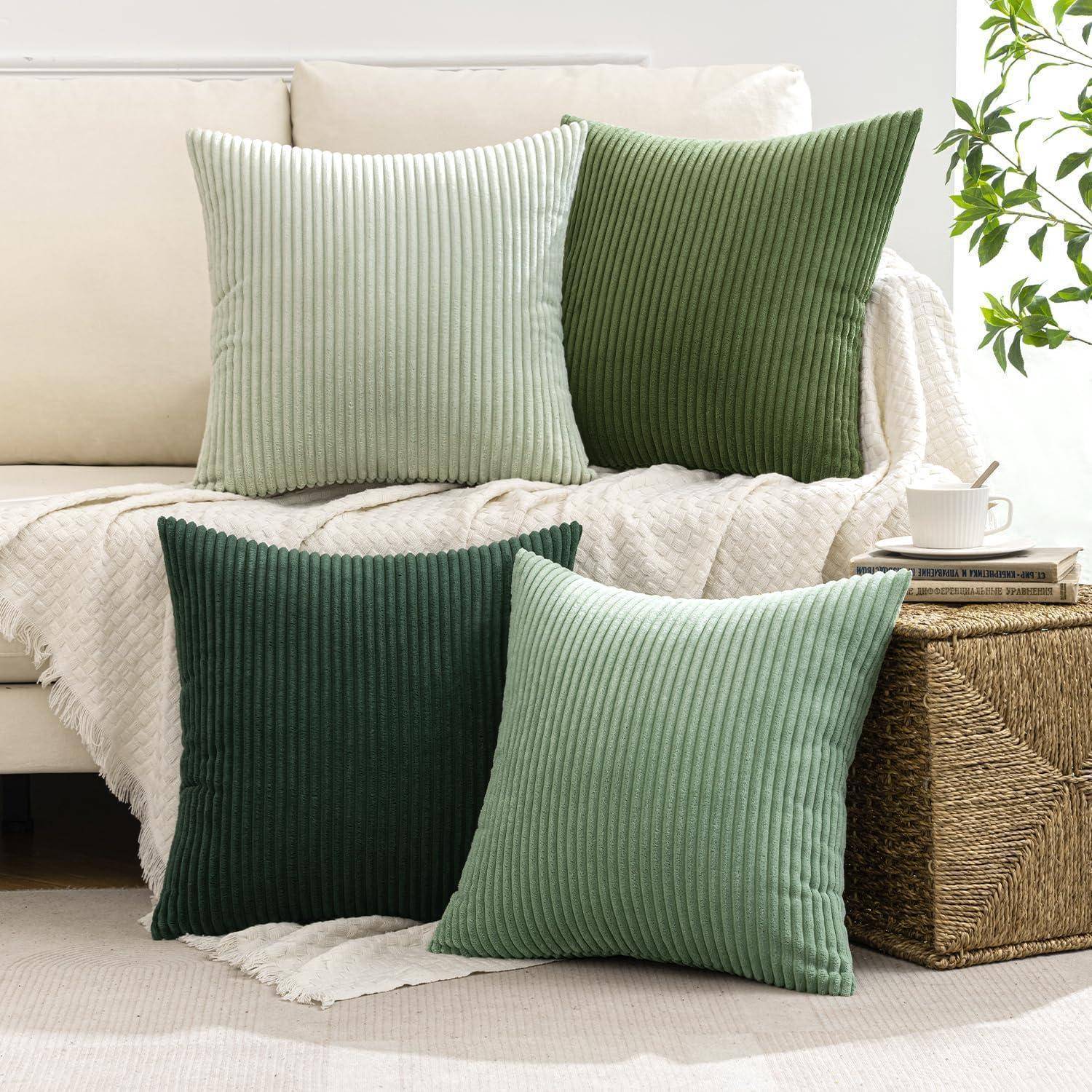 Ein Wohnzimmerambiente mit einem beigen Sofa, das vier quadratische Kissen in verschiedenen Grüntönen aufweist. Ein geflochtener Korbtisch trägt eine kleine Pflanze.