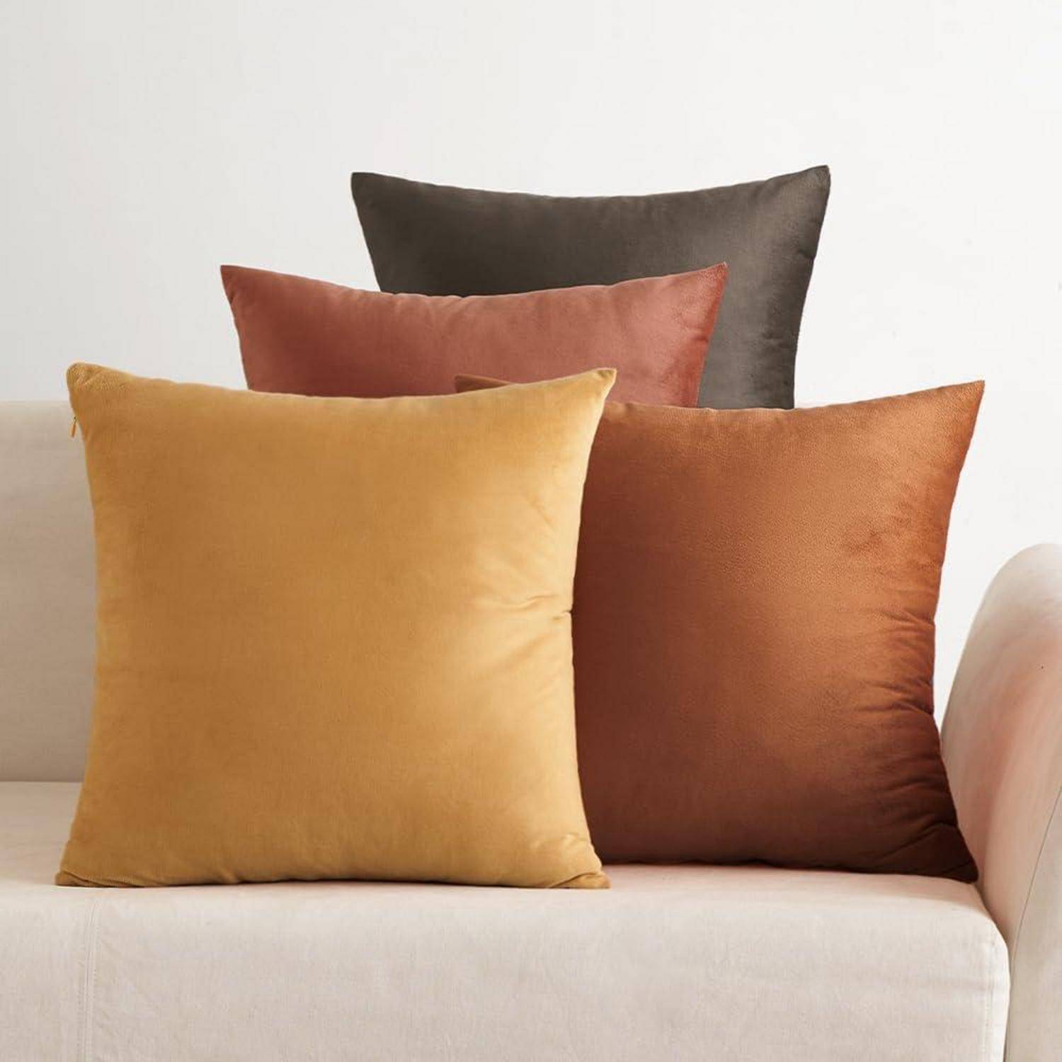 Vier Plüsch-Zierkissen, die auf einem beigen Sofa angeordnet sind und Farben in Senf-Gelb, Burnt Orange und Dunkelbraun aufweisen.
