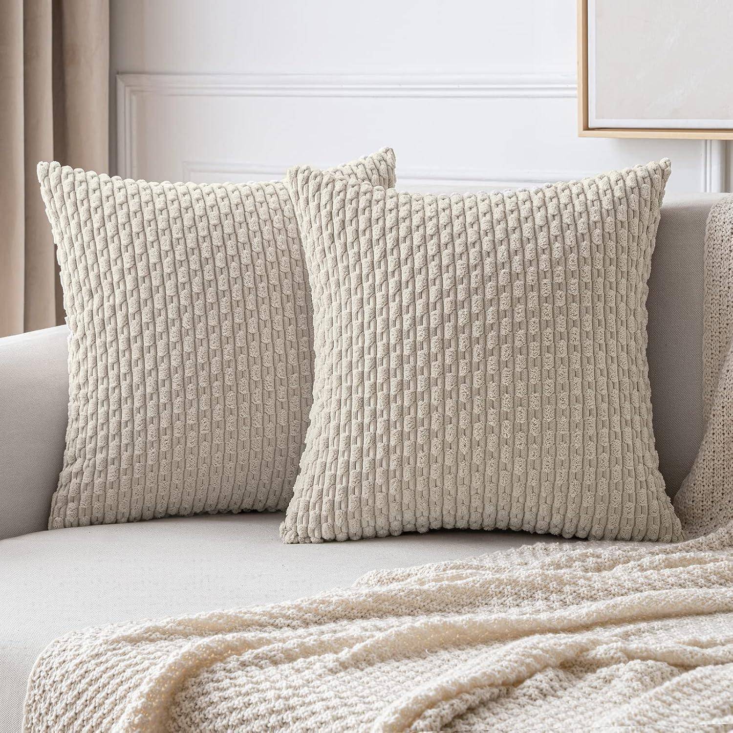 Zwei strukturierte beige Kissen sind auf einem hellgrauen Sofa platziert, ergänzt von einer passenden Decke, die eine gemütliche und neutrale Dekoration schafft.