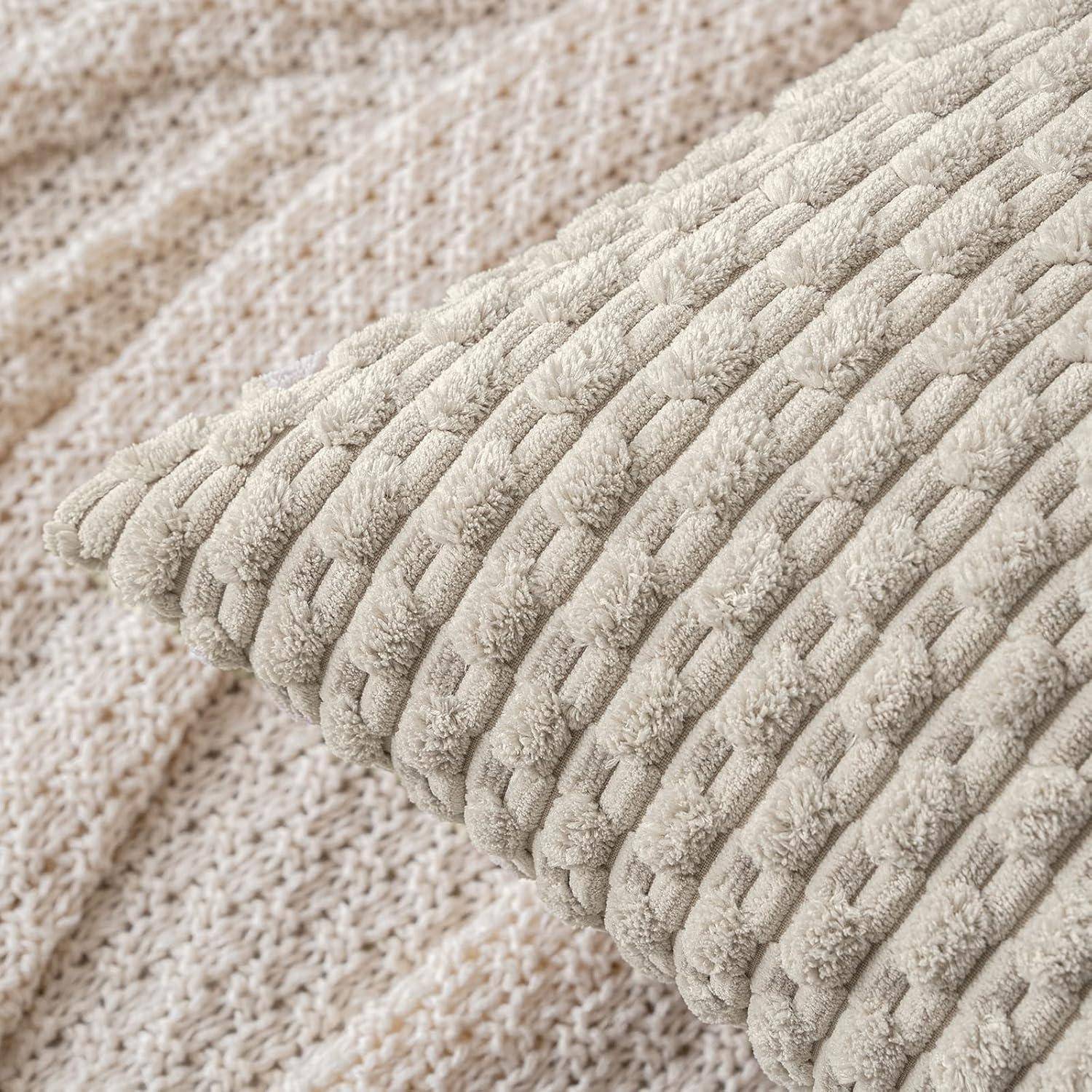 Eine Nahaufnahme eines strukturierten beigen Kissens mit einem geflochtenen Muster, das auf einer gestrickten Stoffoberfläche ruht und eine gemütliche und weiche Atmosphäre vermittelt.