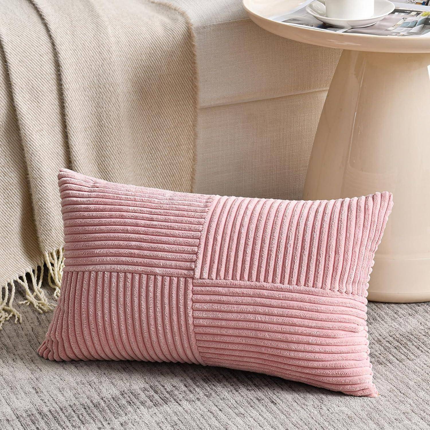 Ein pinker, strukturierter Kissen mit Rippenmuster liegt auf einem grauen Teppich neben einem kleinen, runden weißen Tisch in einer gemütlichen Raumgestaltung.