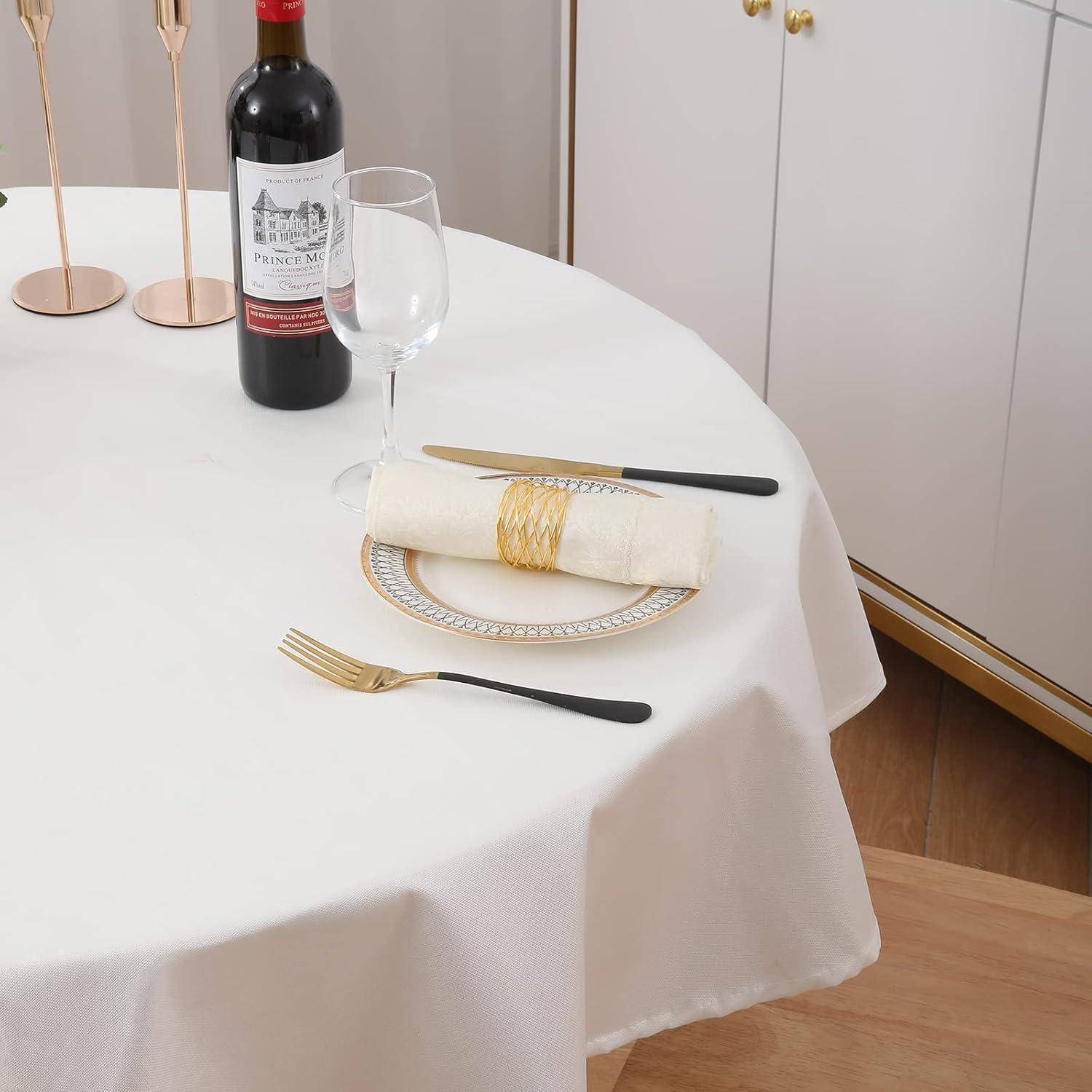 Ein Tisch elegant gedeckt mit einer weißen Tischdecke, auf dem eine Flasche Rotwein, ein Weinglas, goldenes Besteck und ein Teller mit einer gefalteten Serviette platziert sind.