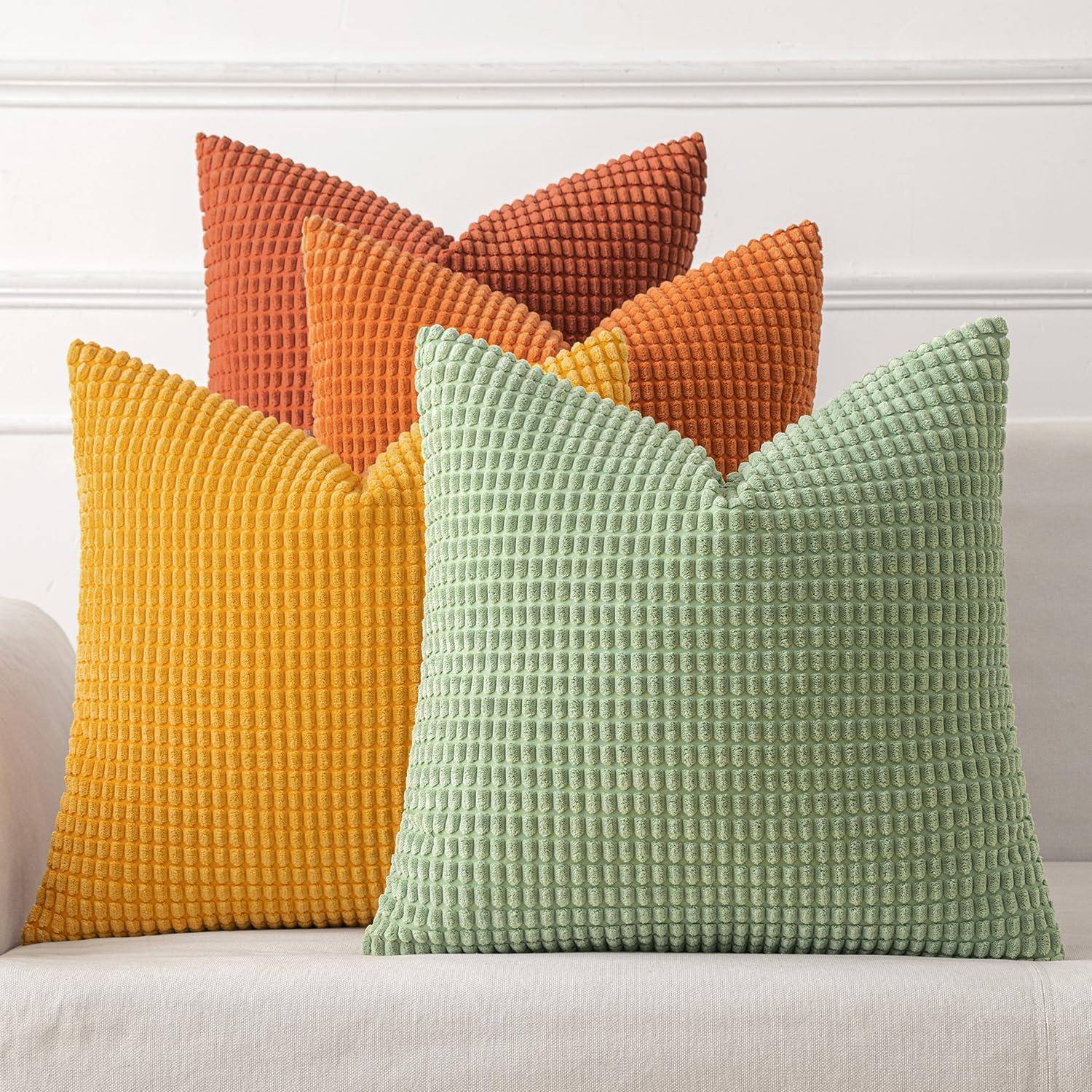 Vier dekorative Kissen mit strukturiertem Stoff in Gelb, Grün, Orange und Rot sind auf einem weißen Sofa vor einer weißen Wand angeordnet.