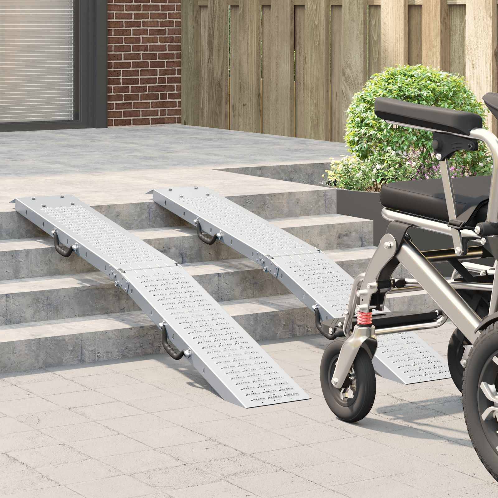 Zwei Metallrollstuhlrampen an Treppenstufen außerhalb eines Gebäudes, die zu einer offenen Tür mit einer Topfpflanze in der Nähe führen.