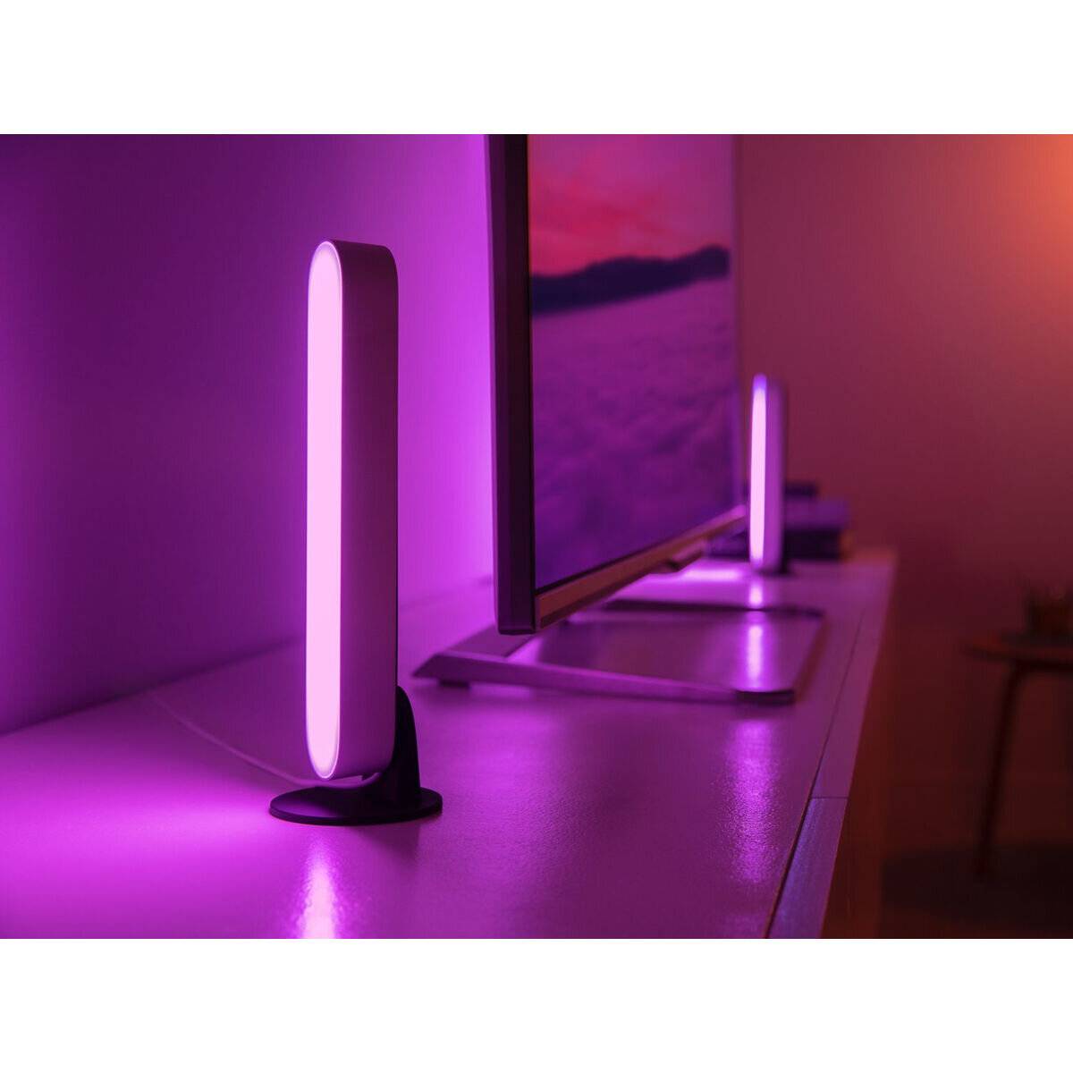 Ein Raum, beleuchtet von violetten LED-Leuchten hinter einem Flachbildschirm, die einen ambientes Leuchten auf einem weißen Schreibtisch erzeugen.