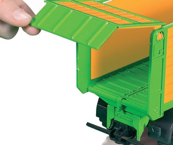 Eine Hand öffnet den Klappdeckel eines kleinen grünen Spielzeugzugs und gibt einen leeren gelben Innenraum frei.