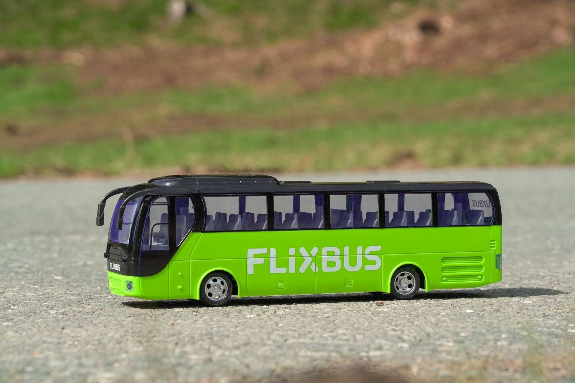 Ein Modell eines grünen FlixBus mit Logo, ruhend auf einer kiesligen Oberfläche, was Reisen oder Transport andeutet.