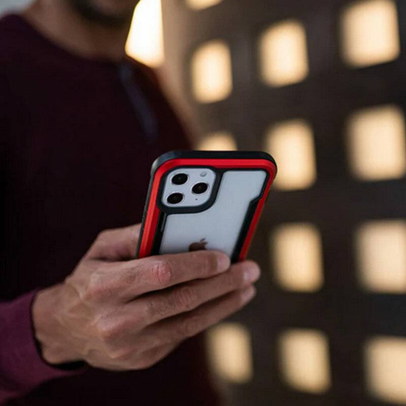 Eine Person hält ein Smartphone mit einer rot-schwarzen Hülle und ist konzentriert auf den Bildschirm fokussiert, was auf eine Beschäftigung mit einem digitalen Gerät hindeutet.