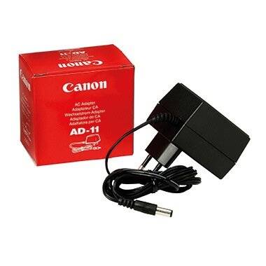 Ein Canon-Netzadapter mit seiner Verpackung. Die Box zeigt das Modell 'AD-11' und präsentiert das Canon-Logo prominent auf einem roten Hintergrund.