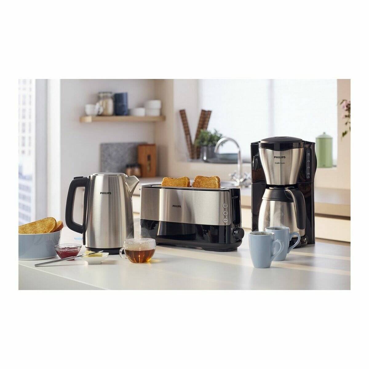Eine Küchenarbeitsplatte zeigt einen Toaster mit getoastetem Brot, einen Wasserkocher, eine Kaffeemaschine und Tassen, was auf die Vorbereitung des Frühstücks hindeutet.