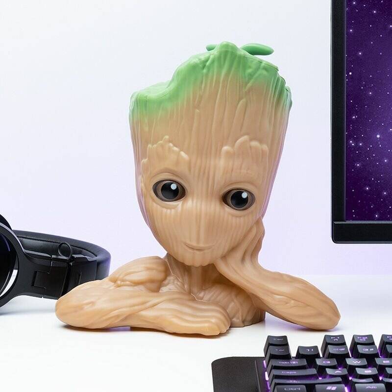 Eine kleine Gestalt, die einem baumartigen Wesen ähnelt, sitzt an einem Schreibtisch und lehnt nachdenklich die Hand an den Kopf. Eine Tastatur und ein Teil eines Monitors sind in der Nähe sichtbar.