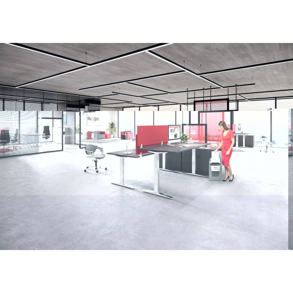 Ein Großraumbüro mit modernen Schreibtischen und Trennwänden. Eine Person in Rot benutzt einen Aktenvernichter in der Nähe eines Schreibtischs. Helle und geräumige Inneneinrichtung.