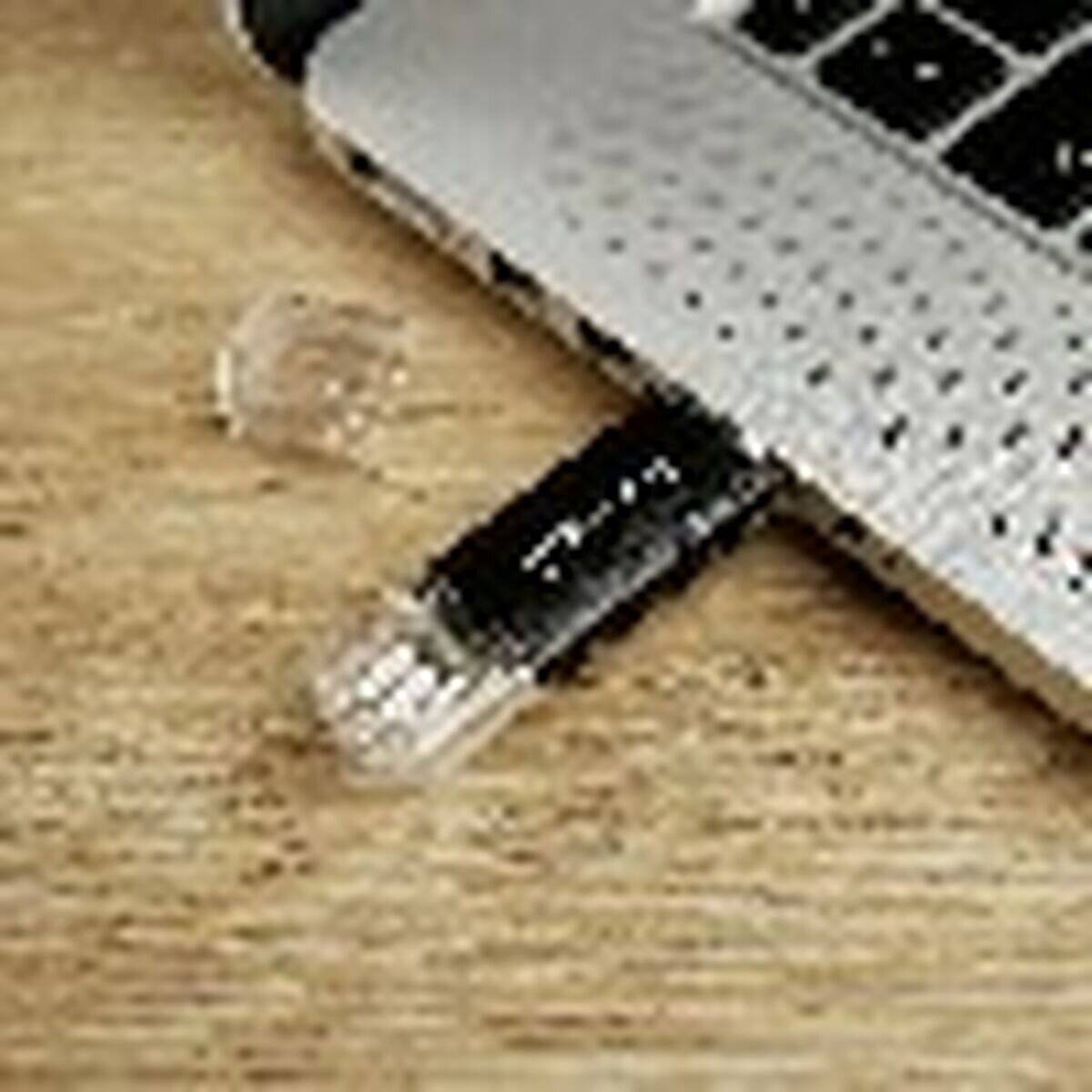 Ein USB-Stick steckt teilweise in einem silbernen Laptop auf einer Holzoberfläche.