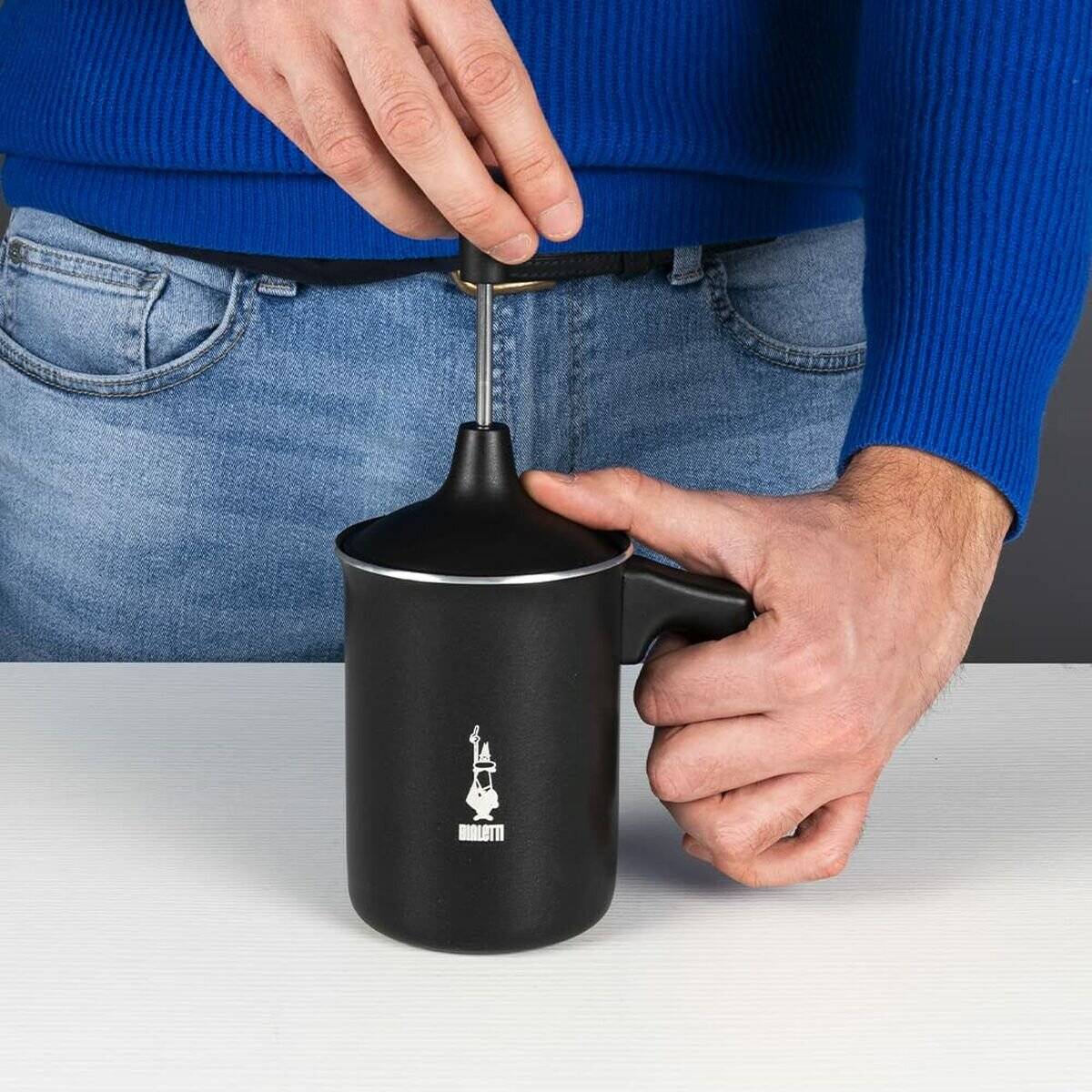 Hände, die einen Stempelaufsatz über einer schwarzen Kaffeetasse mit einem Logo darauf halten, bereit zum Kaffeeaufguss.