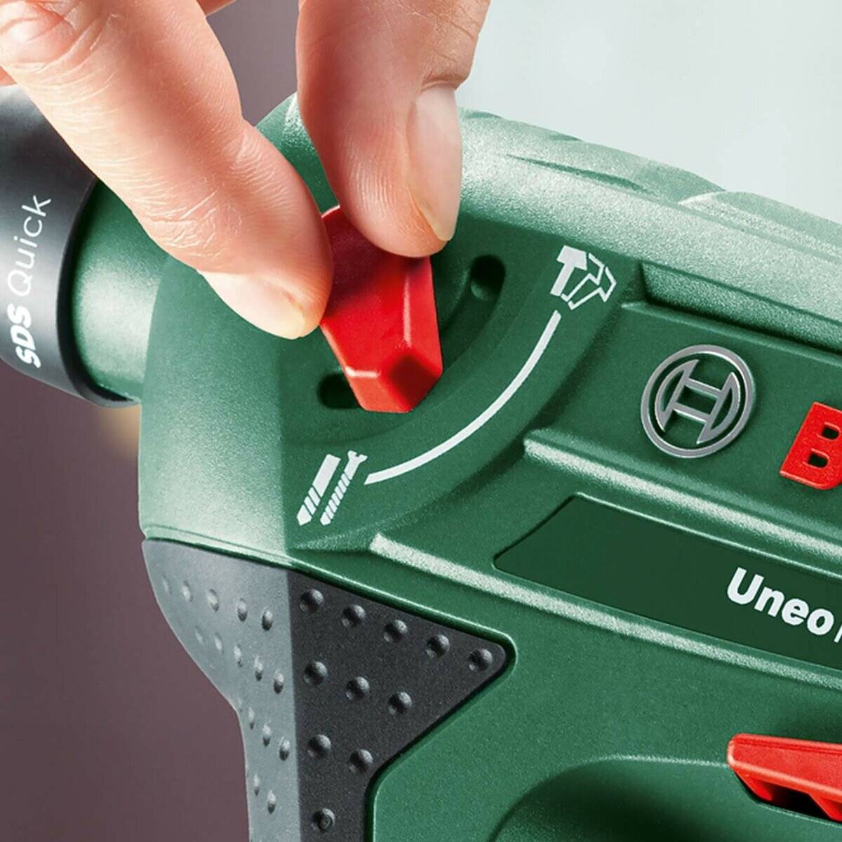 Nahaufnahme einer Hand, die einen roten Schalter an einem grünen Elektrowerkzeug mit der Aufschrift „SDS Quick