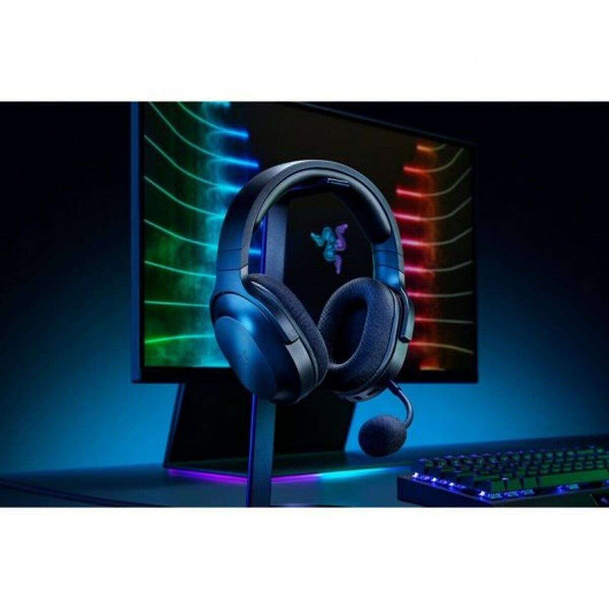 Ein Gaming-Headset mit Mikrofon wird auf einem Ständer vor einem Monitor präsentiert, der farbenfrohe Lichtmuster zeigt, neben einer Tastatur.