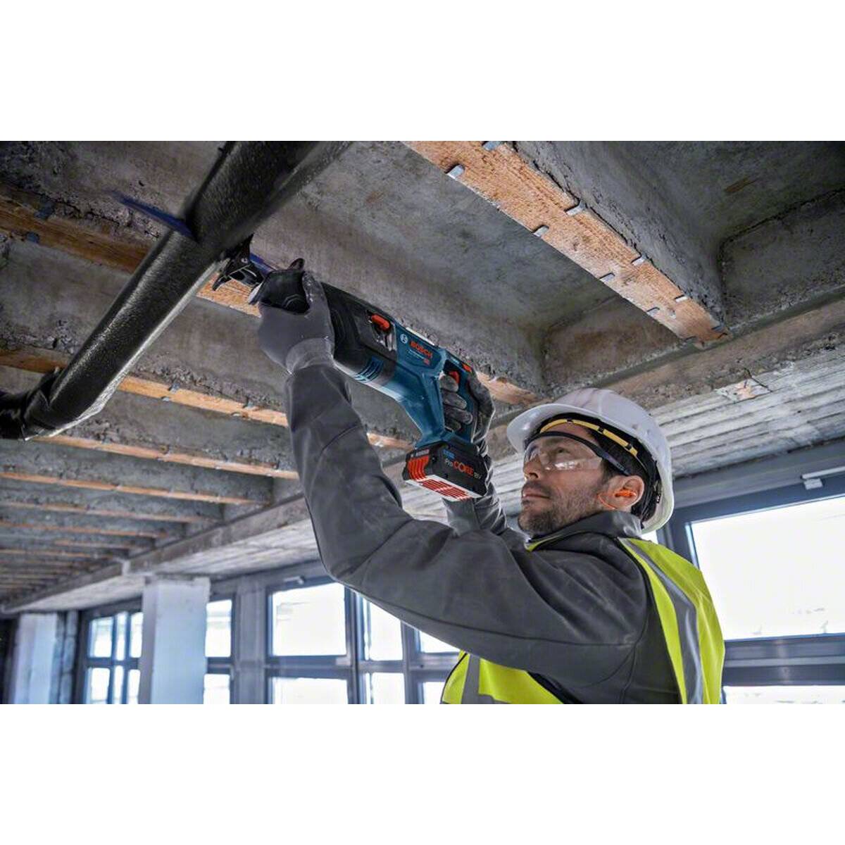 Ein Bauarbeiter in einer Sicherheitsweste und einem Schutzhelm verwendet ein Elektrowerkzeug, um ein Metallrohr auf einer Baustelle zu durchtrennen.