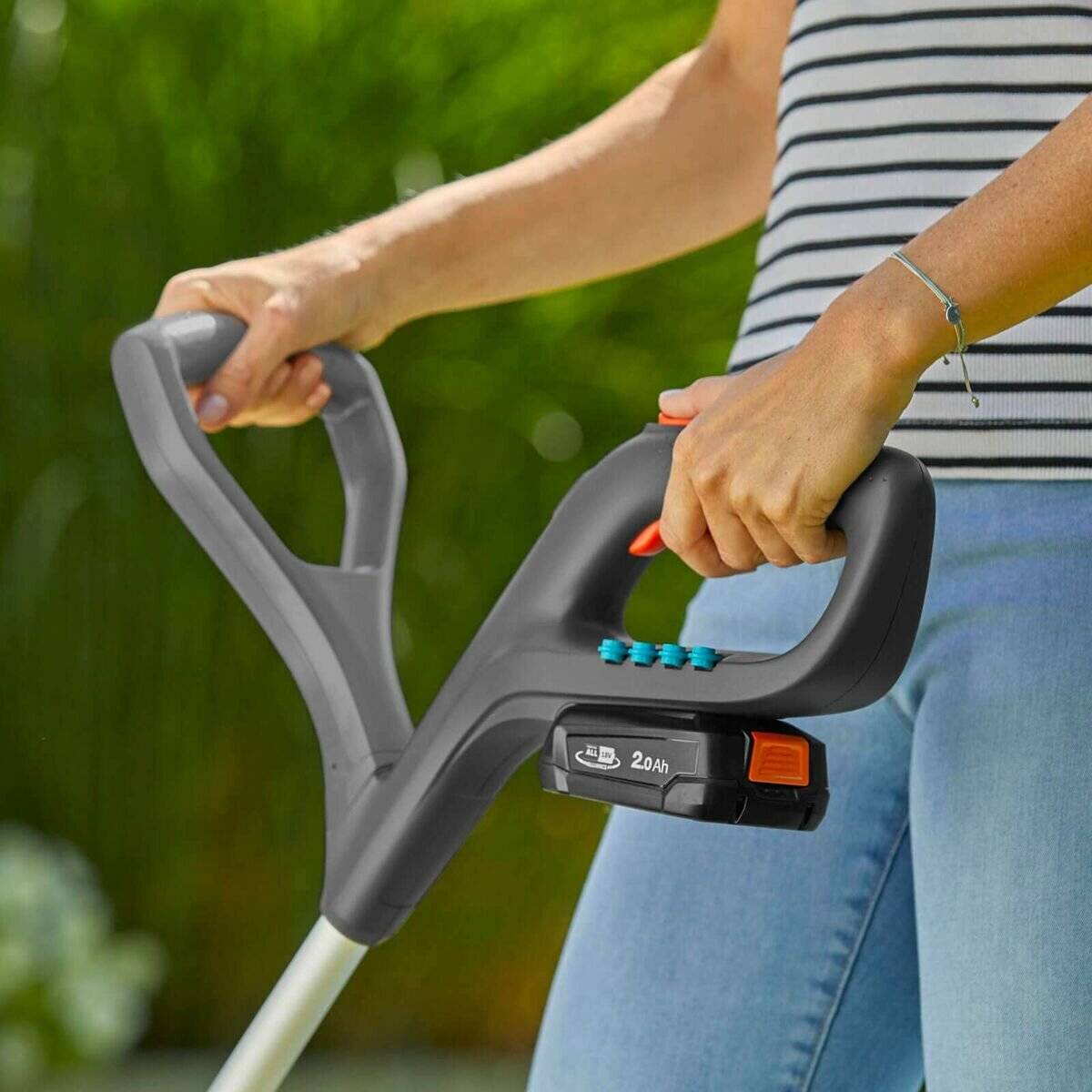 Eine Person hält den Griff eines kabellose Gartengeräts mit Batterieanzeigelichtern, das eine Kapazität von 20Ah in einer Gartenumgebung zeigt.
