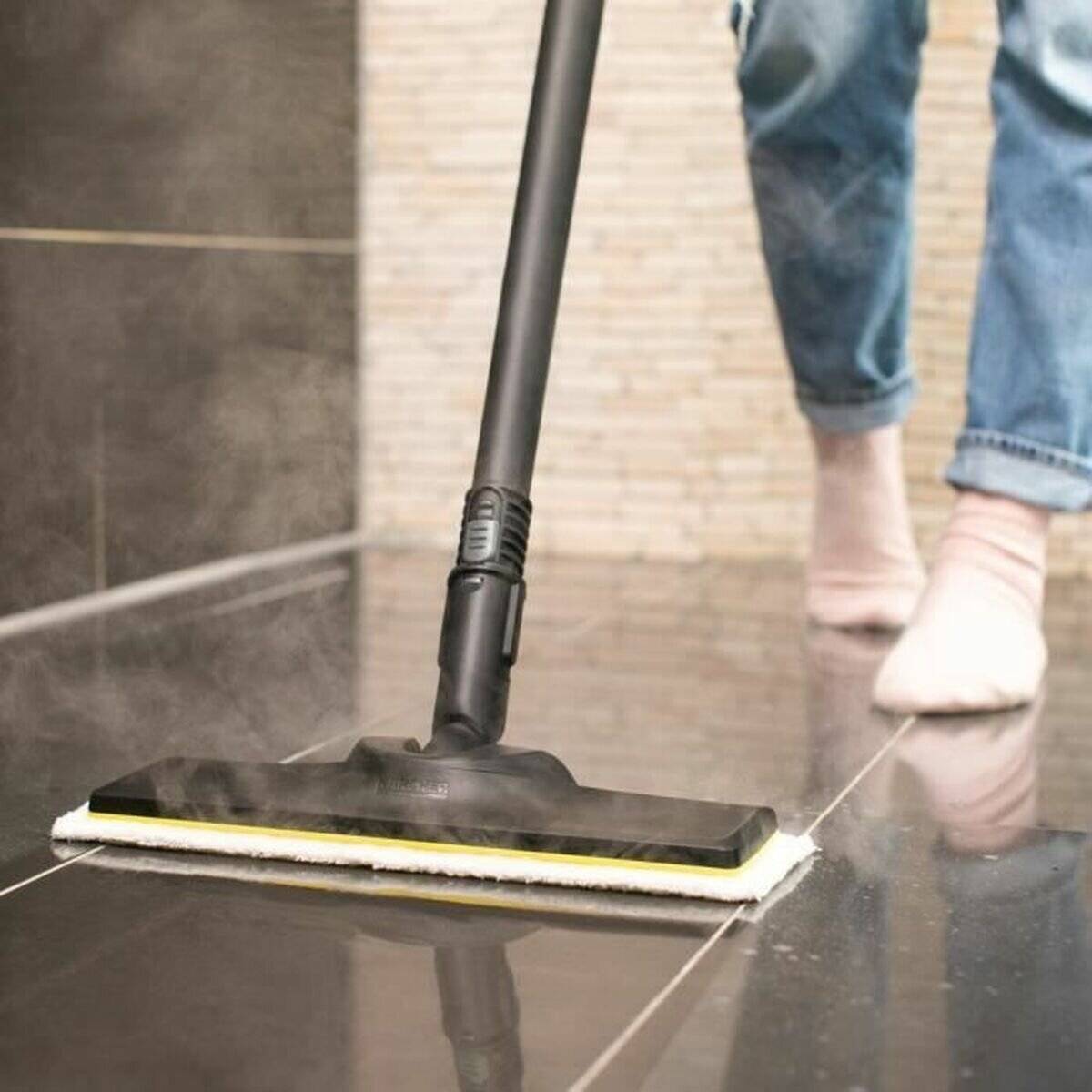 Eine Person mit hochgerollten Jeans benutzt einen Dampfmopp, um einen glänzenden gefliesten Boden zu reinigen, wobei Dampf um den Moppkopf herum sichtbar ist.