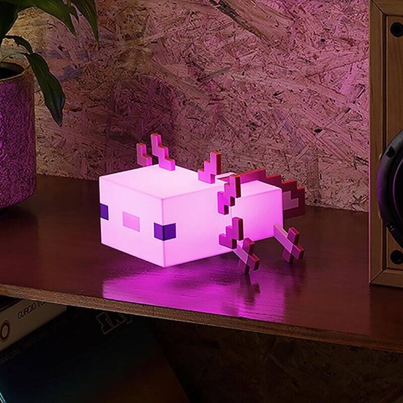 Eine verpixelte Axolotl-Nachtlampe verbreitet ein rosa Leuchten auf einem Holzregal, neben einem Lautsprecher und einer Topfpflanze, und erzeugt eine gemütliche Atmosphäre.