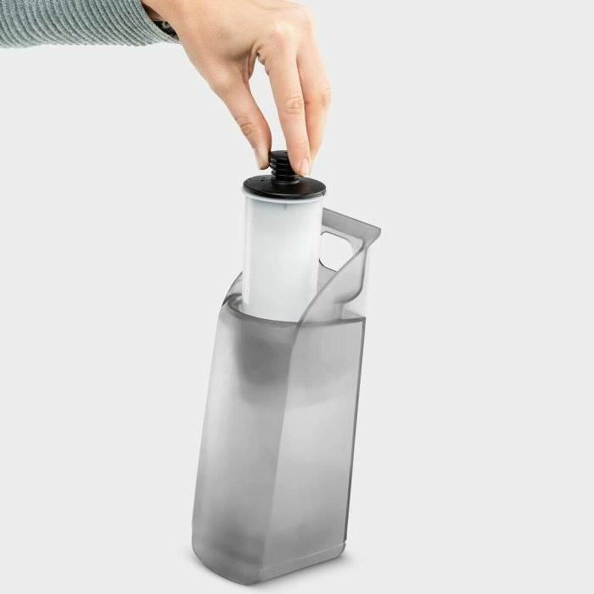 Eine Hand hält einen Kohlefilter, der in einen transparenten Wasserkrug eingesetzt wird und dabei seine Filtrationsfunktion betont.