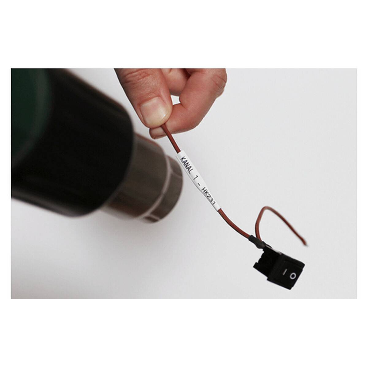 Eine Hand hält einen beschrifteten Kabelverbinder, dessen Beschriftung lautet ‚Kanal 1 – Heizung'. Der Verbinder ist schwarz mit roten Kabeln.