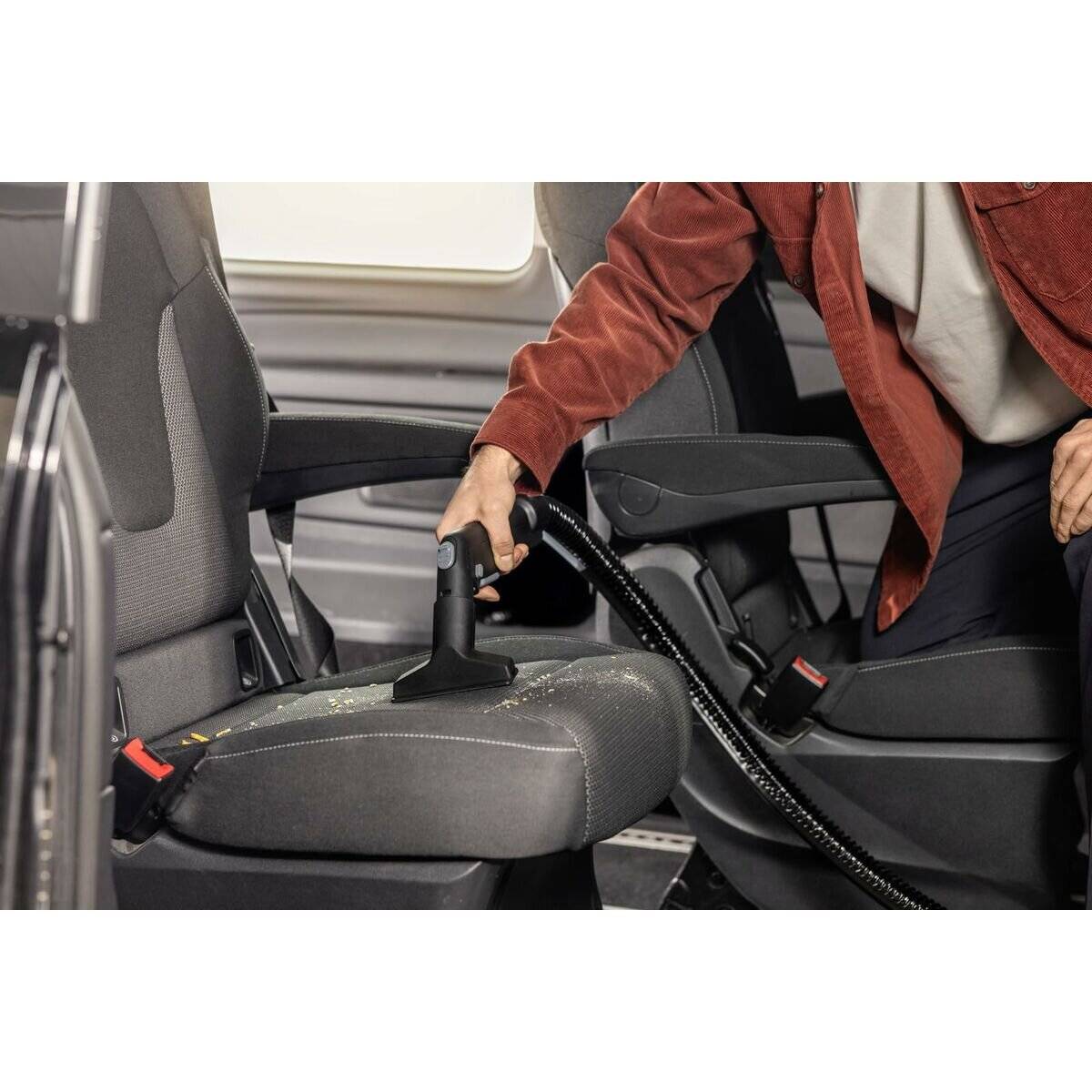 Eine Person benutzt ein Saugaufsatz, um den Sitz eines Fahrzeugs zu reinigen und sich dabei darauf zu konzentrieren, Schmutz und Ablagerungen zu entfernen.