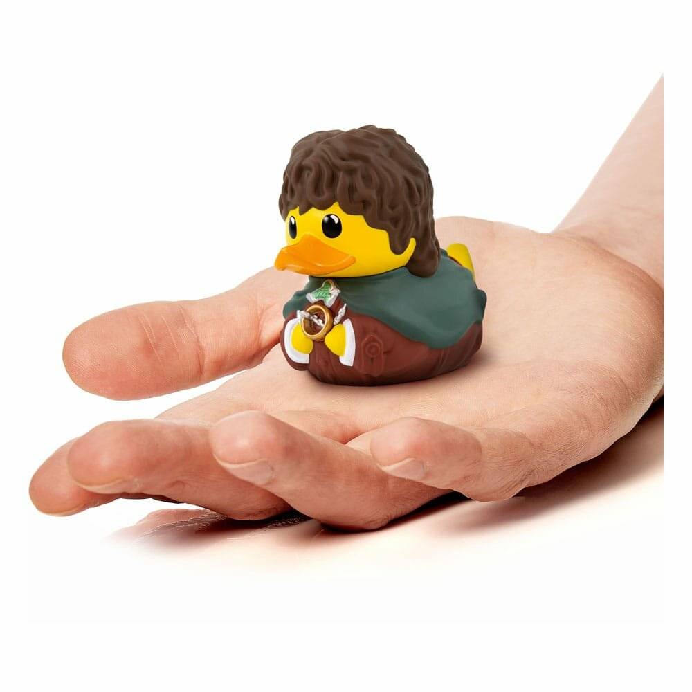 Eine Hand, die eine kleine, gelbe Gummiente hält, die in Fantasie-Kleidung gekleidet ist und einem Charakter mit lockigem braunem Haar und einem grünen Umhang ähnelt.