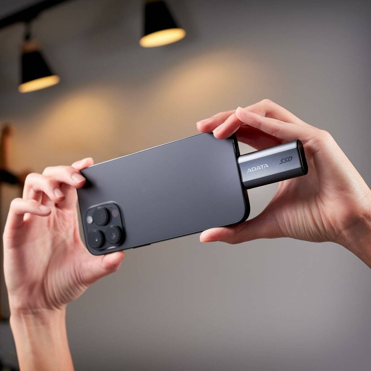 Eine Person hält ein Smartphone mit einer externen SSD, die angesteckt ist, und demonstriert mobile Datenspeicherung.