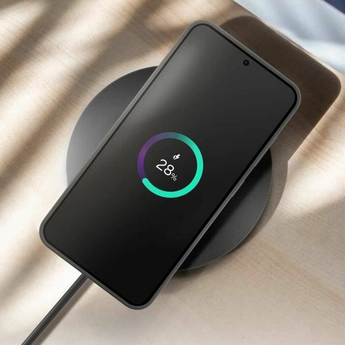 Ein Smartphone auf einem drahtlosen Ladegerät zeigt ein Batterieladesymbol mit 28% Ladung.