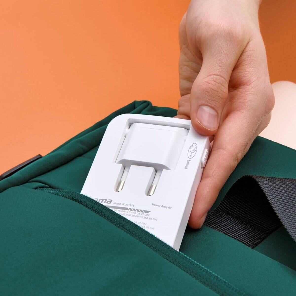 Eine Person legt ein weißes Netzteil in die Seitentasche eines grünen Rucksacks, was die Vorbereitung auf eine Reise oder tägliche Aktivitäten andeutet.