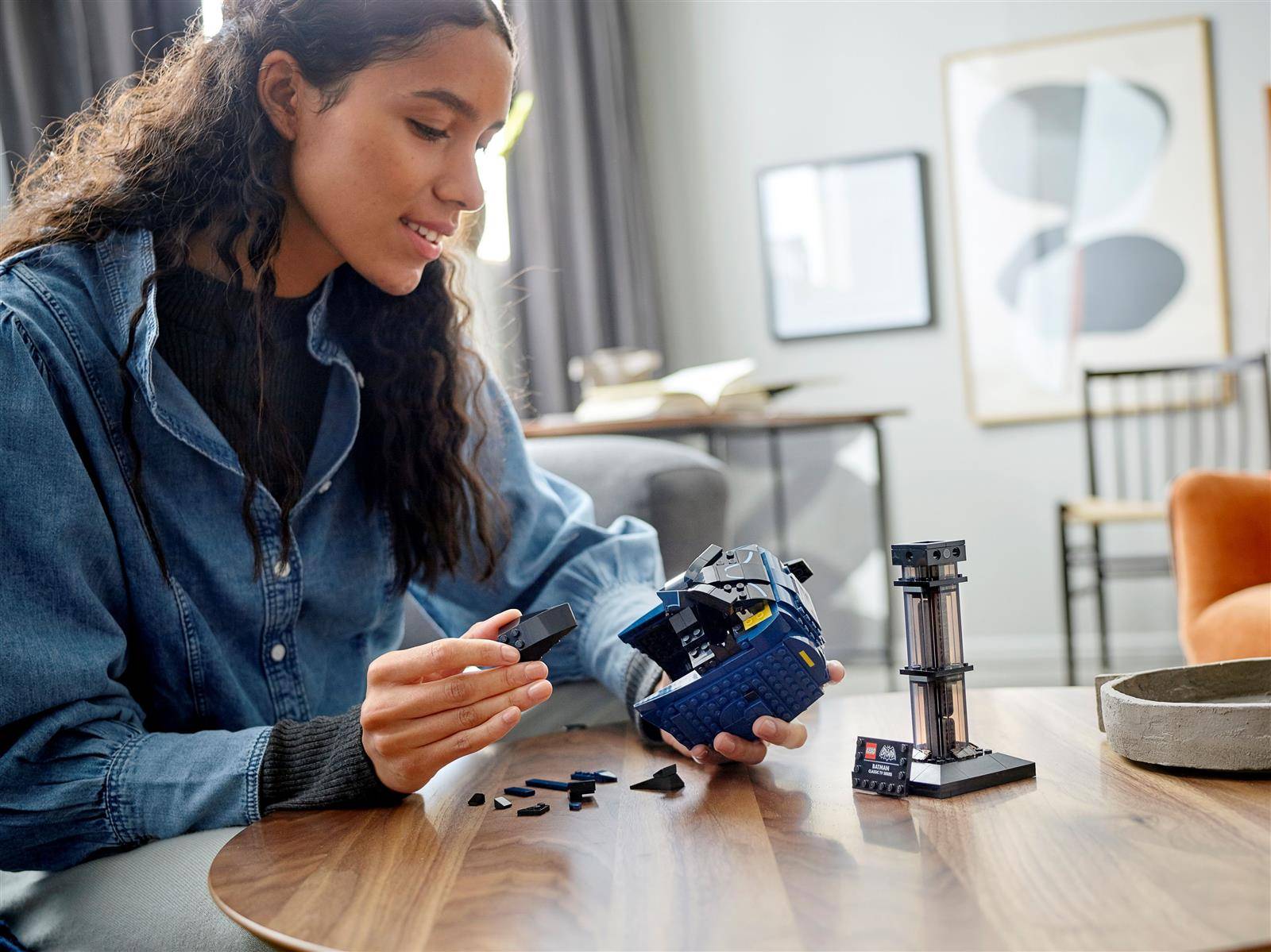 Eine Person, die an einem Tisch einen LEGO-Satz zusammenbaut und sich dabei auf ein sphärisches Modell konzentriert, mit weiteren Bausteinen und einer kleinen Struktur in der Nähe, in einem modernen Raum.