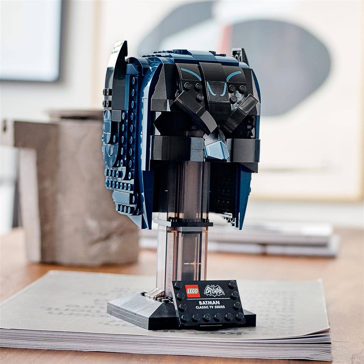 LEGO Batman Maske, auf einem Tisch ausgestellt; mit präzisen Details und einem Namensschild im Vordergrund, auf dem 