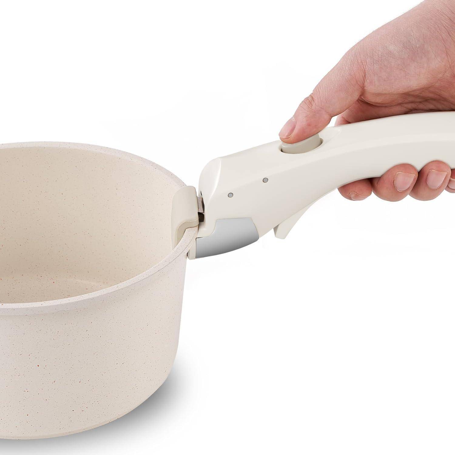 Eine Hand, die einen weißen Kochtopf mit beigefarbener Innenseite hält und dessen Griff-Druckmechanismus zeigt. Der Kochtopf ist leer.