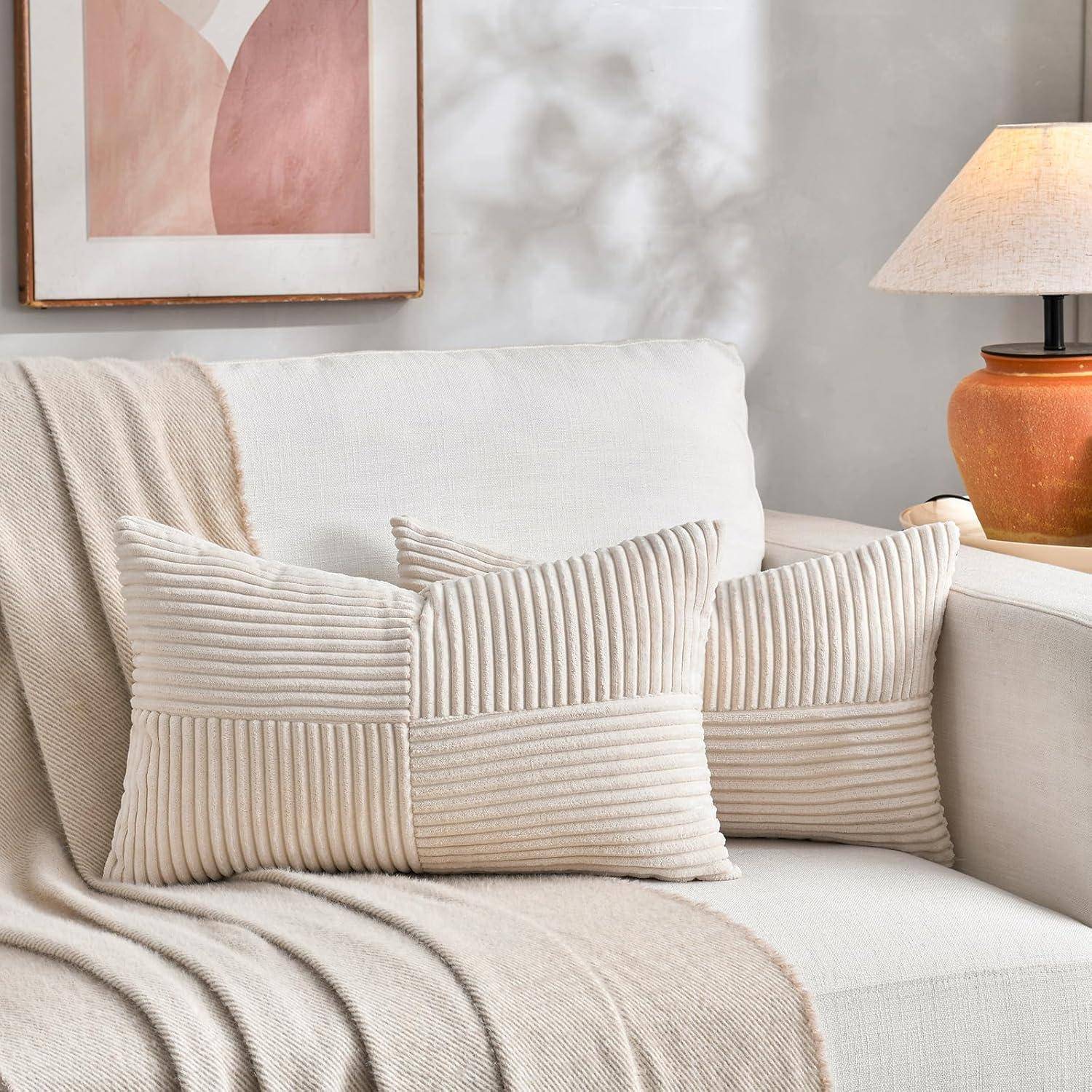 Ein gemütliches Wohnzimmer mit einem weißen Sofa, beigen strukturierten Kissen und einer weichen Decke. Eine Lampe und abstrakte Kunstwerke unterstreichen die Ästhetik.