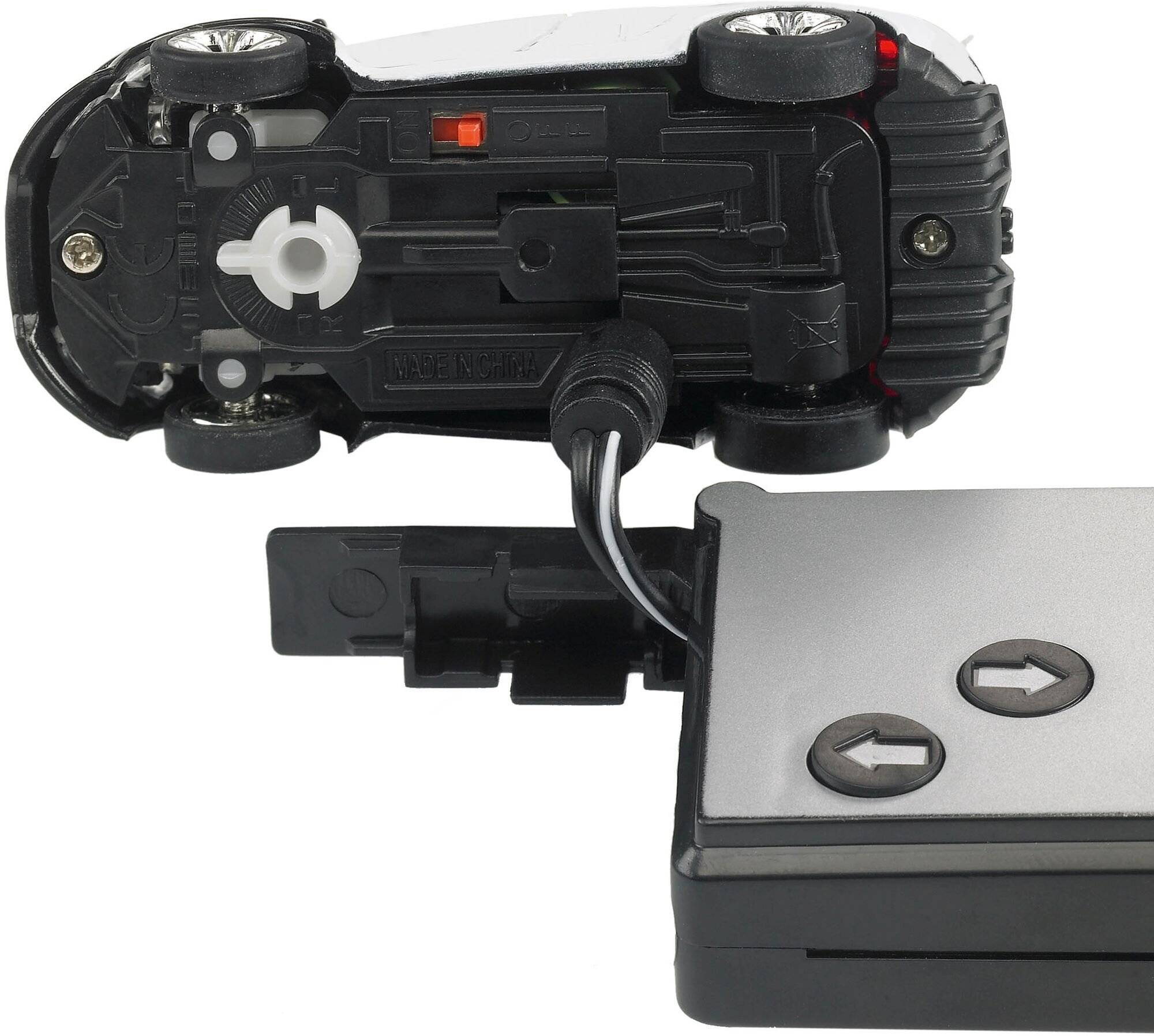 Ein kleines Spielzeugauto ist auf den Kopf gestellt, wobei sein Untergestell sichtbar ist, und mit einem rechteckigen Controller durch ein Kabel verbunden.