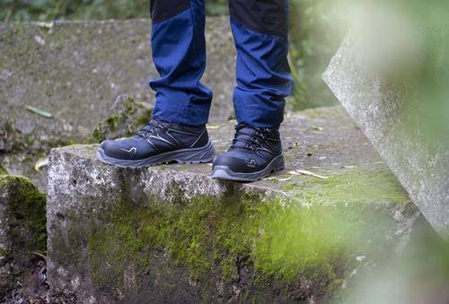 Eine Person, die blaue Wanderhosen und schwarze Wanderstiefel trägt, steht auf einer moosigen Steinoberfläche in einer natürlichen Outdoor-Umgebung.