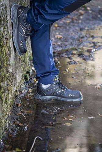 „Eine Person in blauen Wanderstiefeln und Hosen steht in einer Pfütze auf einem felsigen Weg und deutet damit auf eine Outdoor-Aktivität unter nassen Bedingungen hin.