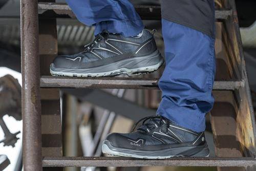 Eine Person in blauen Hosen und schwarzen Turnschuhen steigt eine Metalltreppe hinauf und konzentriert sich dabei auf robustes Schuhwerk, das für Outdoor-Aktivitäten geeignet ist.