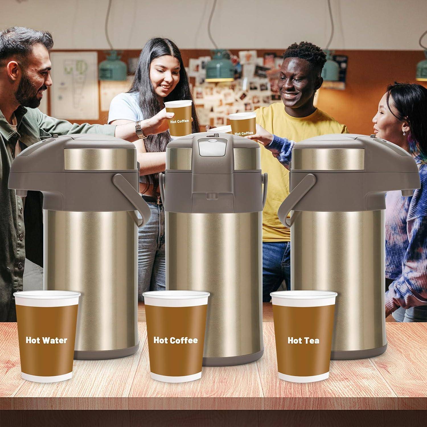 Menschen versammeln sich um einen Tisch mit Thermospendern für heißes Wasser, heißen Kaffee und heißen Tee, wobei jeder Spender mit beschrifteten Tassen versehen ist.