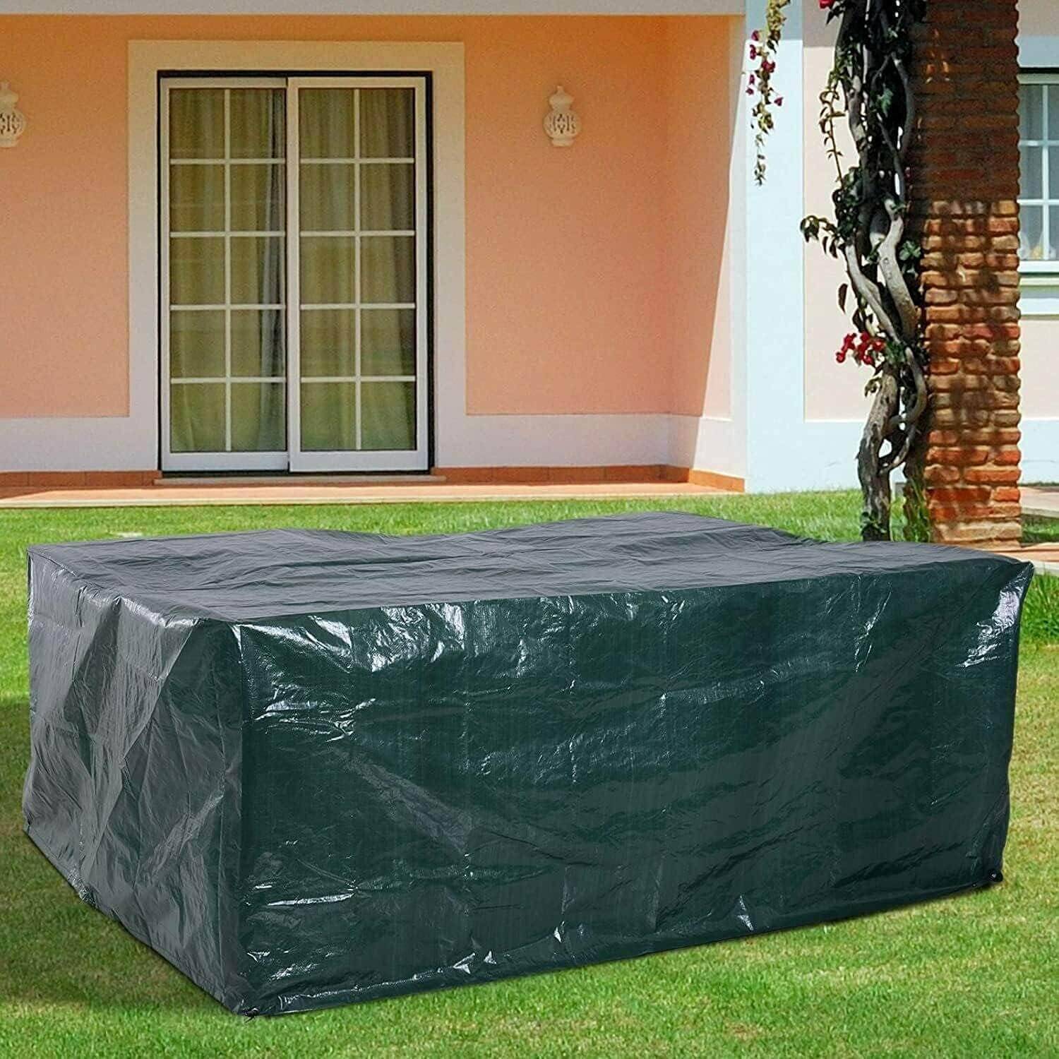 Eine große, dunkelgrüne Gartenmöbel-Abdeckung, die einen Tisch und Stühle auf einem Rasengrund schützt, mit einem Haus und Terrassentüren im Hintergrund.