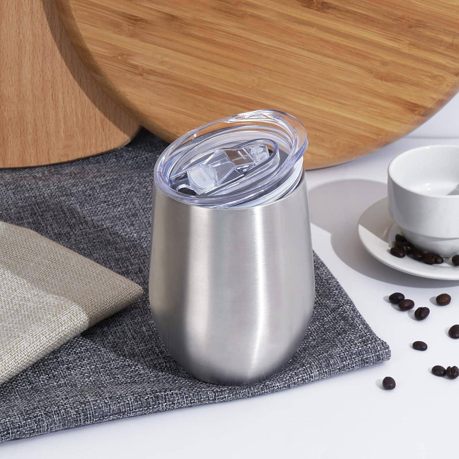 Ein Thermobecher aus Edelstahl mit Deckel steht auf einem grauen Tuch, neben einer weißen Tasse und verstreuten Kaffeebohnen, mit Holzbrettern im Hintergrund.