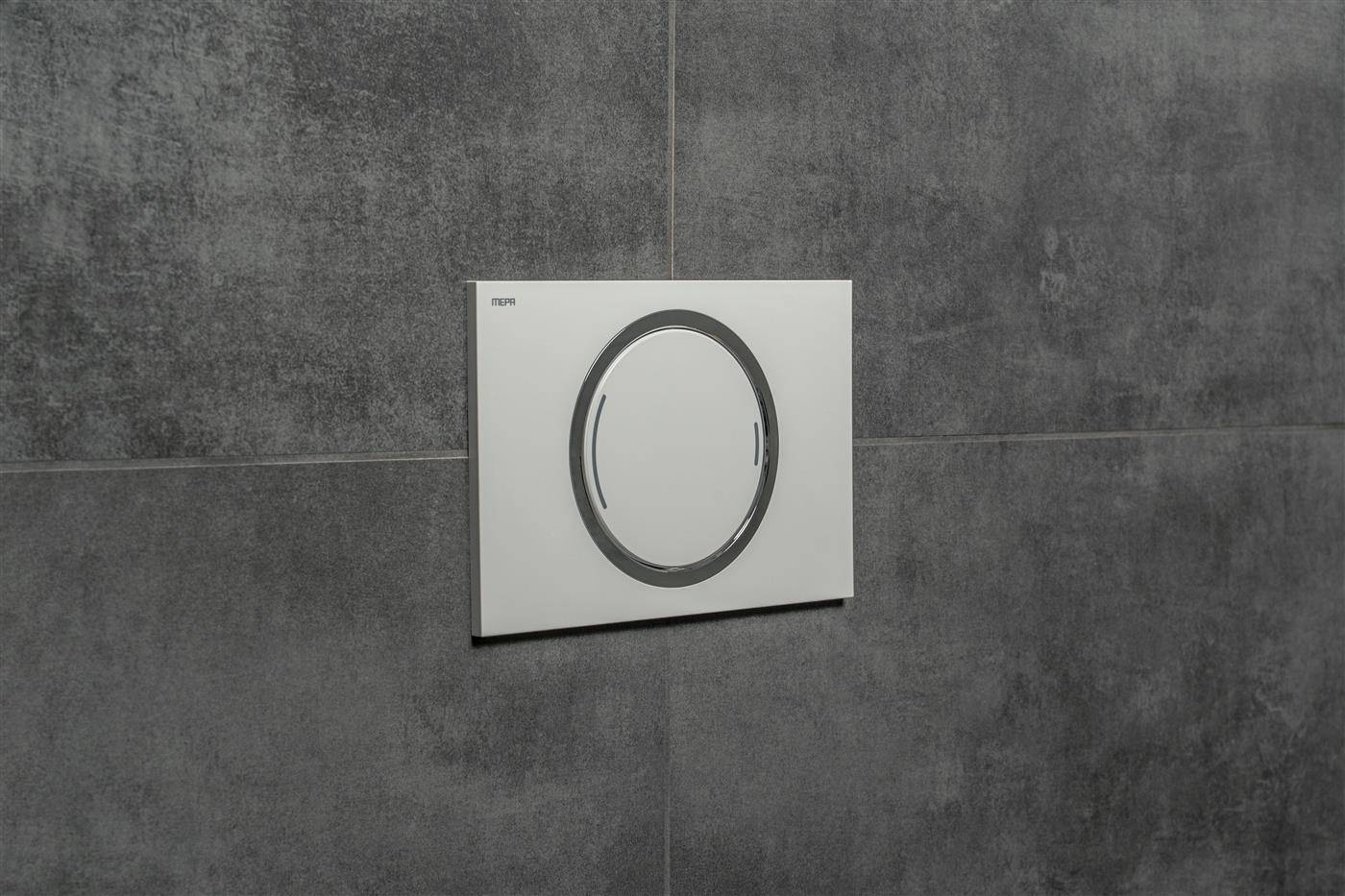 Weiße, bündig montierte Bedienfeld-Platte mit großem kreisförmigem Ringknopf auf einer grau gefliesten Wand.