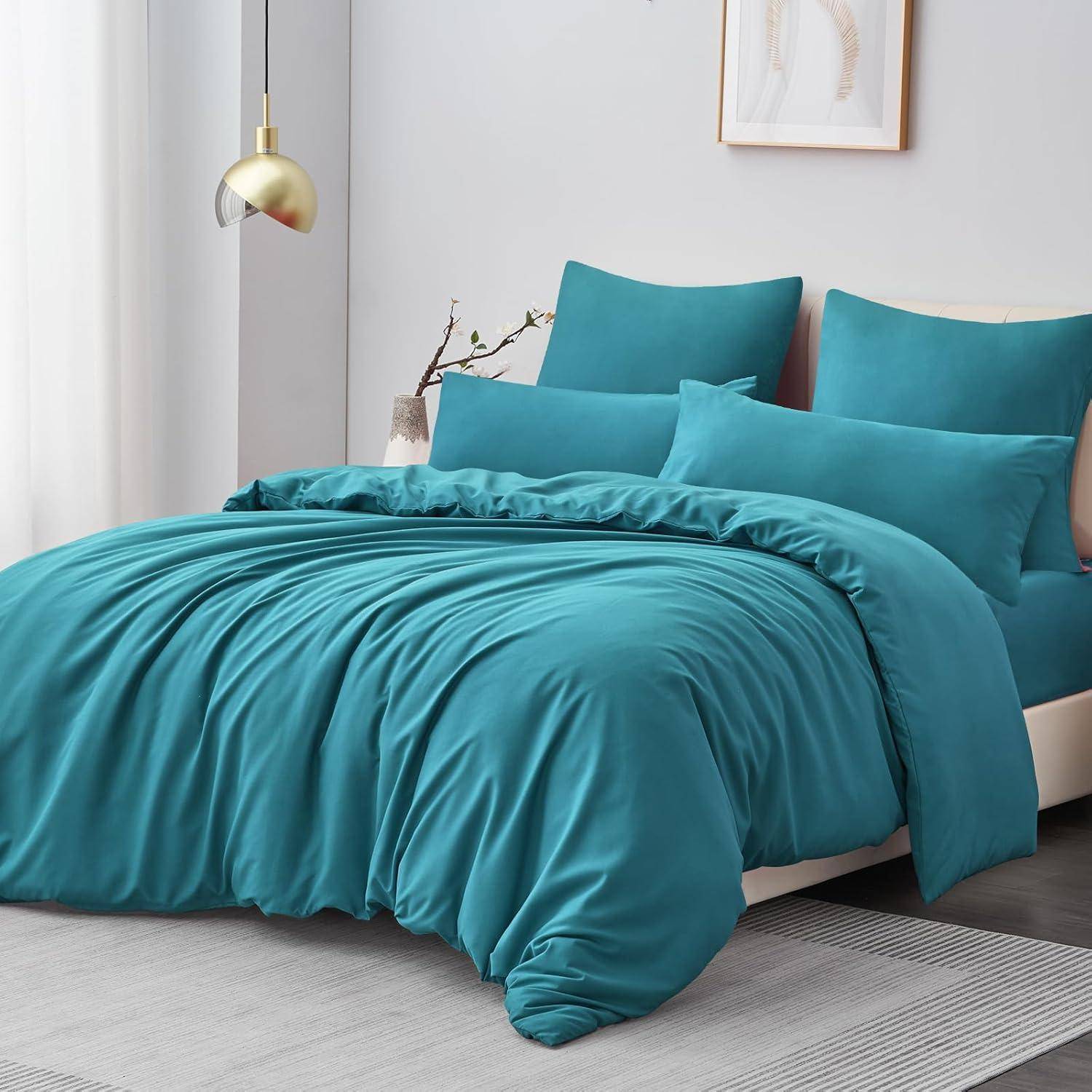 Ein ordentlich gemachtes Bett mit Peacock-Blau-Bettwäsche und Kissen in einem modernen Schlafzimmer. Eine goldene Wandlampe und gerahmte Kunstwerke ergänzen die Dekoration.