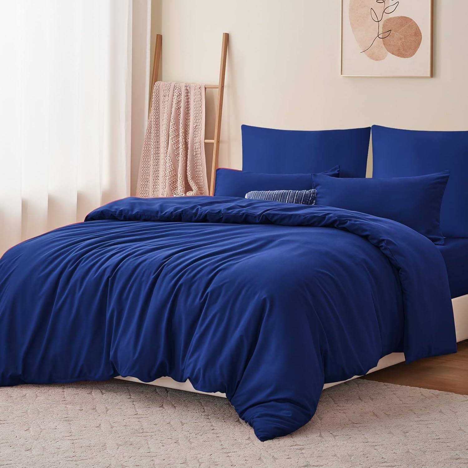 Ein ordentlich gemachtes Bett mit tiefdunkler blauer Bettwäsche, einschließlich Kissen, Laken und einer Bettdecke, in einem neutral gefärbten Raum.