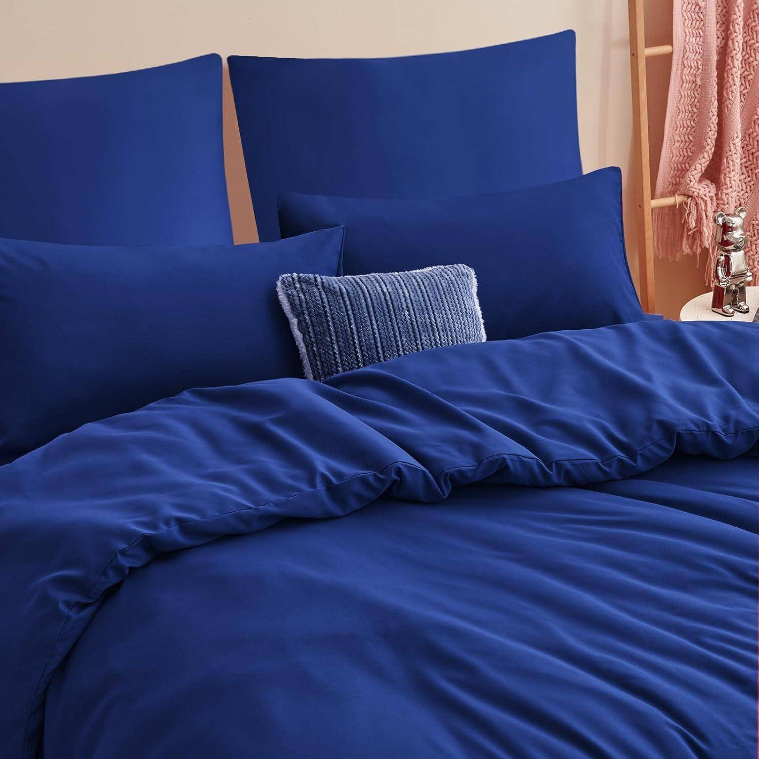 Ein Bett mit tiefdunkelblauen Laken und Kissen, ein gestreiftes Zierkissen in der Mitte und eine gestrickte rosa Decke, die seitlich drapiert ist.
