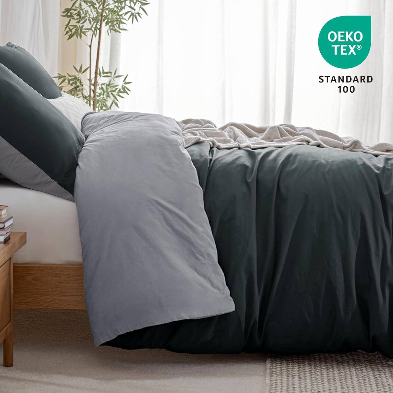 Ein sorgfältig bezogenes Bett mit dunkelgrüner und hellgrauer Bettwäsche, neben einem Holznachttisch. Im Hintergrund ist eine Pflanze zu sehen. Das 'OEKO-TEX STANDARD 100' Etikett befindet sich in der oberen rechten Ecke.