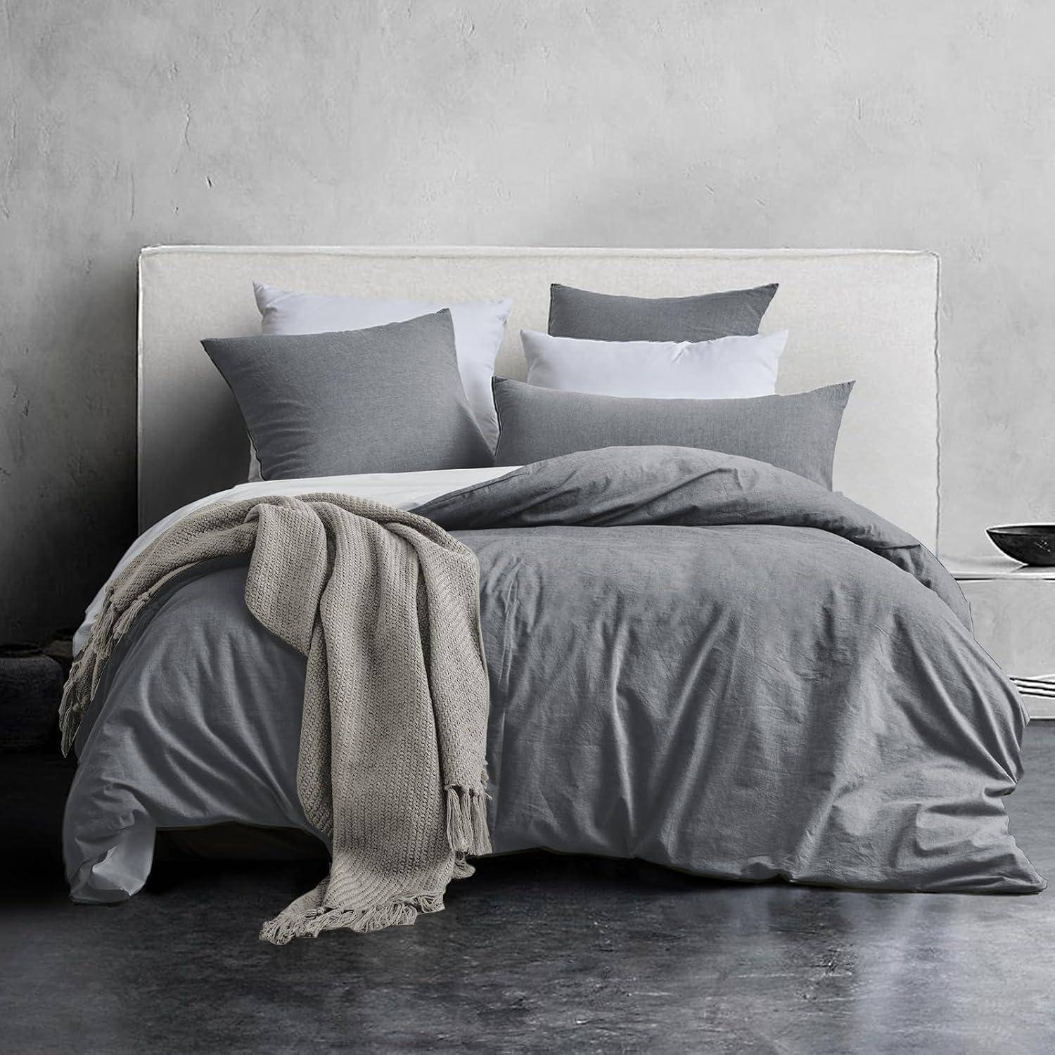 Ein ordentlich gemachtes Bett mit grauer Bettwäsche, einschließlich Bettdecke und Kissen, wird durch eine beige Decke ergänzt, die seitlich über das Bett drapiert ist.