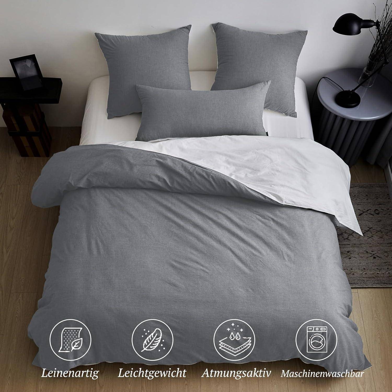 Ein ordentlich gemachtes Bett mit grauer Bettwäsche, einschließlich Kissen, Bettdecke und Bettdeckenbezug. Icons darunter heben Merkmale hervor: leinen-ähnlich, leicht, atmungsaktiv und maschinell waschbar.
