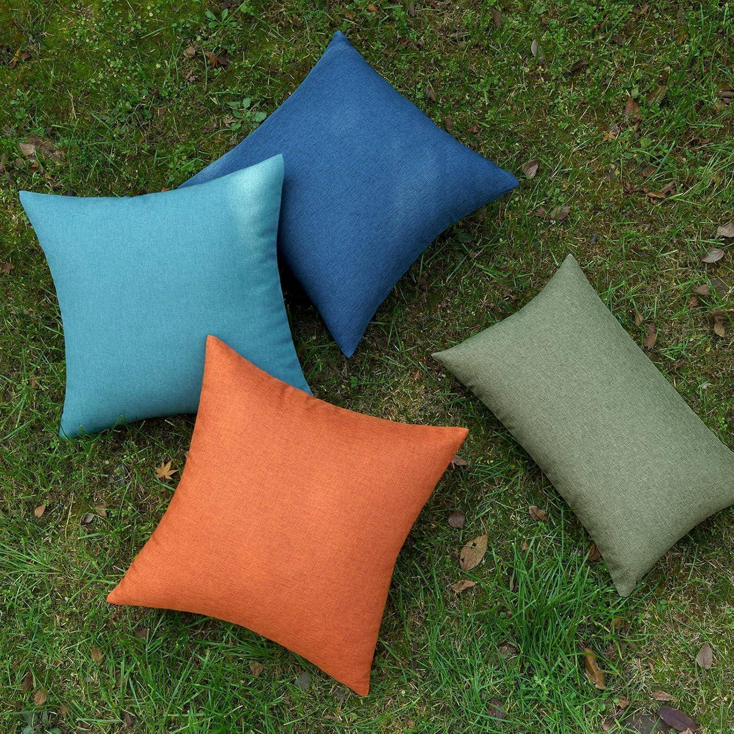 Vier Kissen in Blau, Orange und zwei Schattierungen von Grün sind auf Gras angeordnet und deuten eine lässige Outdoorsituation an.